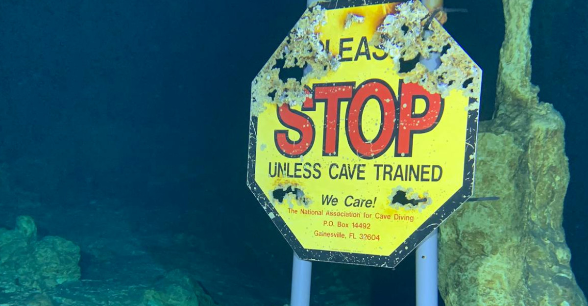 Underwater cave environment with a warning sign for divers to ensure safety before proceeding