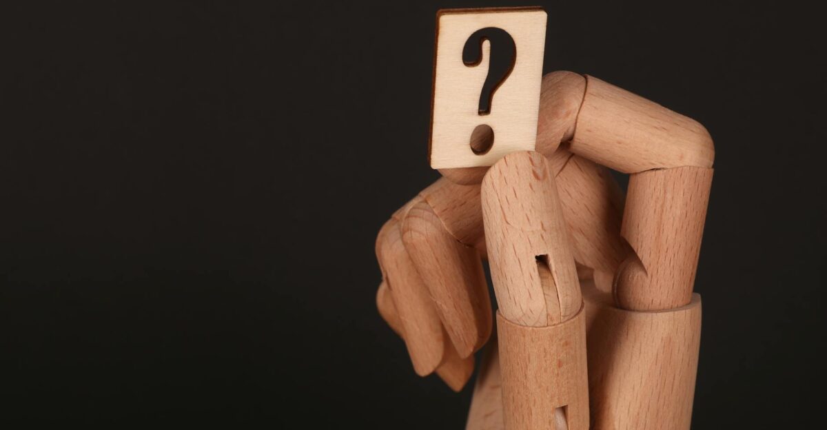 Close-up of a wooden mannequin hand holding a block with a question mark emphasizing curiosity