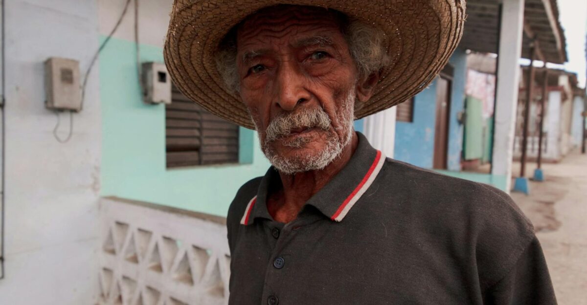 Portrait of a senior man wearing a straw hat standing outside a house