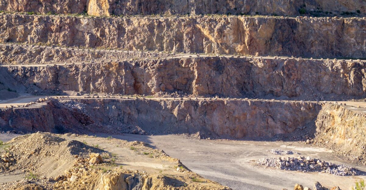 Sunlit view of a rugged multi-layered rock quarry with exposed strata and rocky terrain