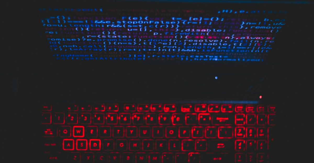Dark-themed laptop setup with a red glowing keyboard and code on screen ideal for tech enthusiasts