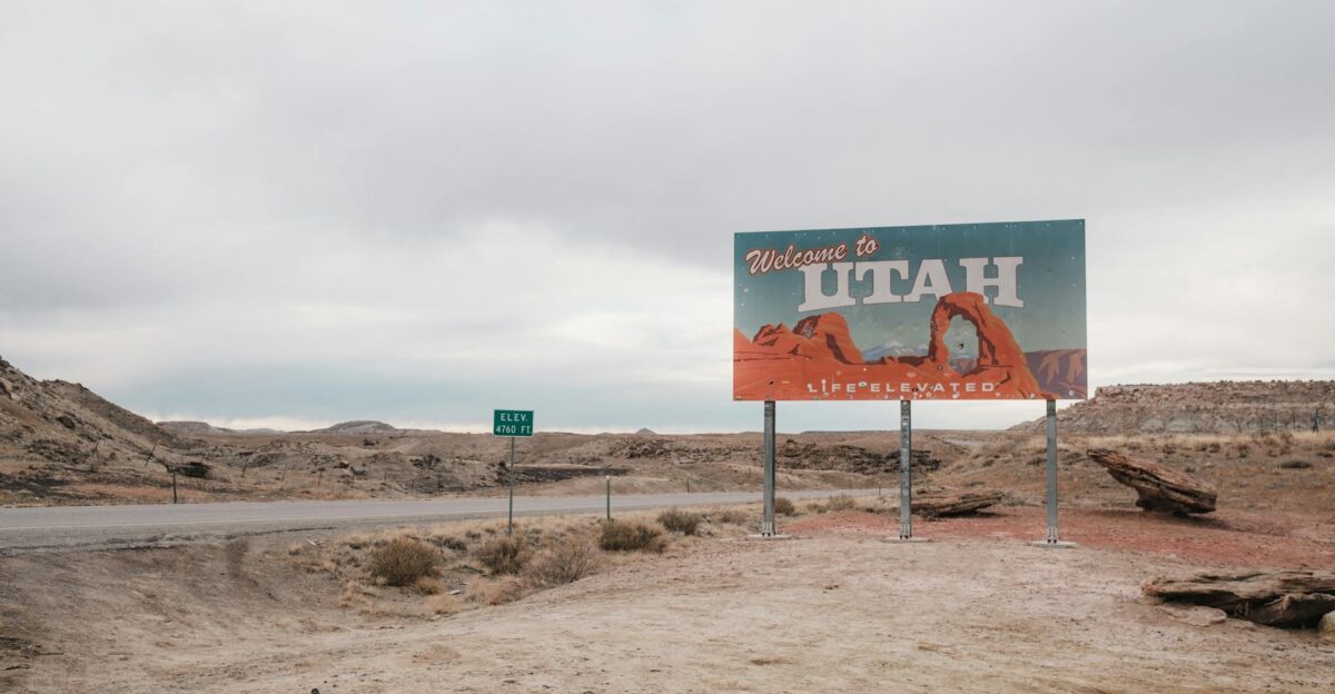 A Welcome to Utah sign with desert landscape background under a cloudy sky