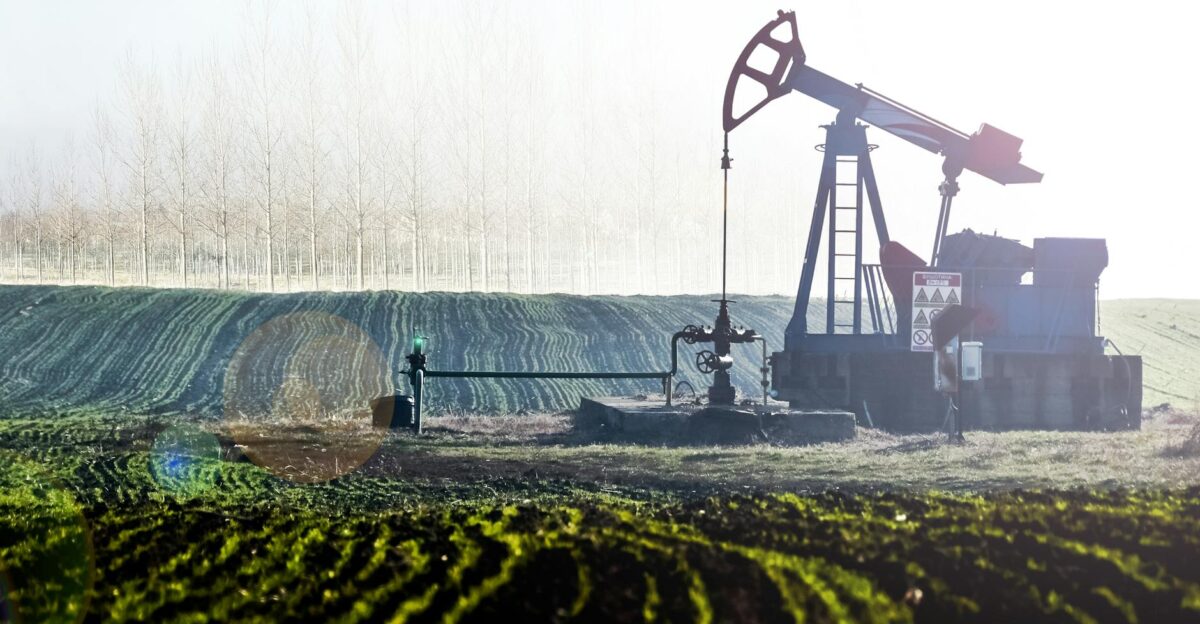 Oil pumpjack in scenic agricultural landscape with lush fields and distant trees