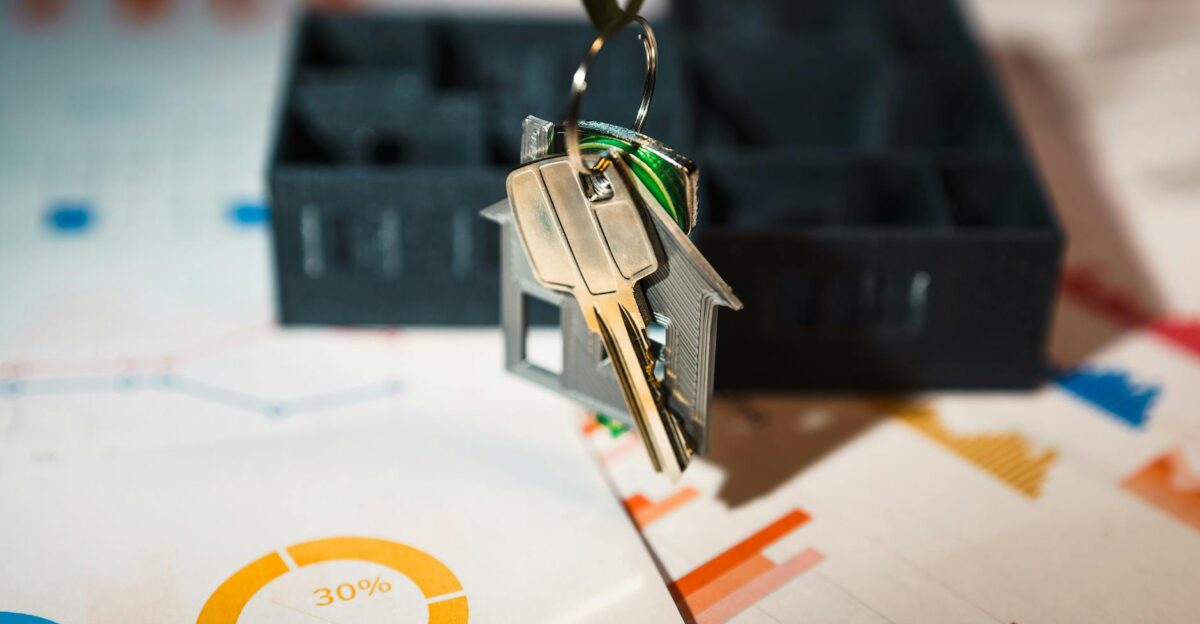 Real estate keys on house keychain with financial graphs symbolizing property investment