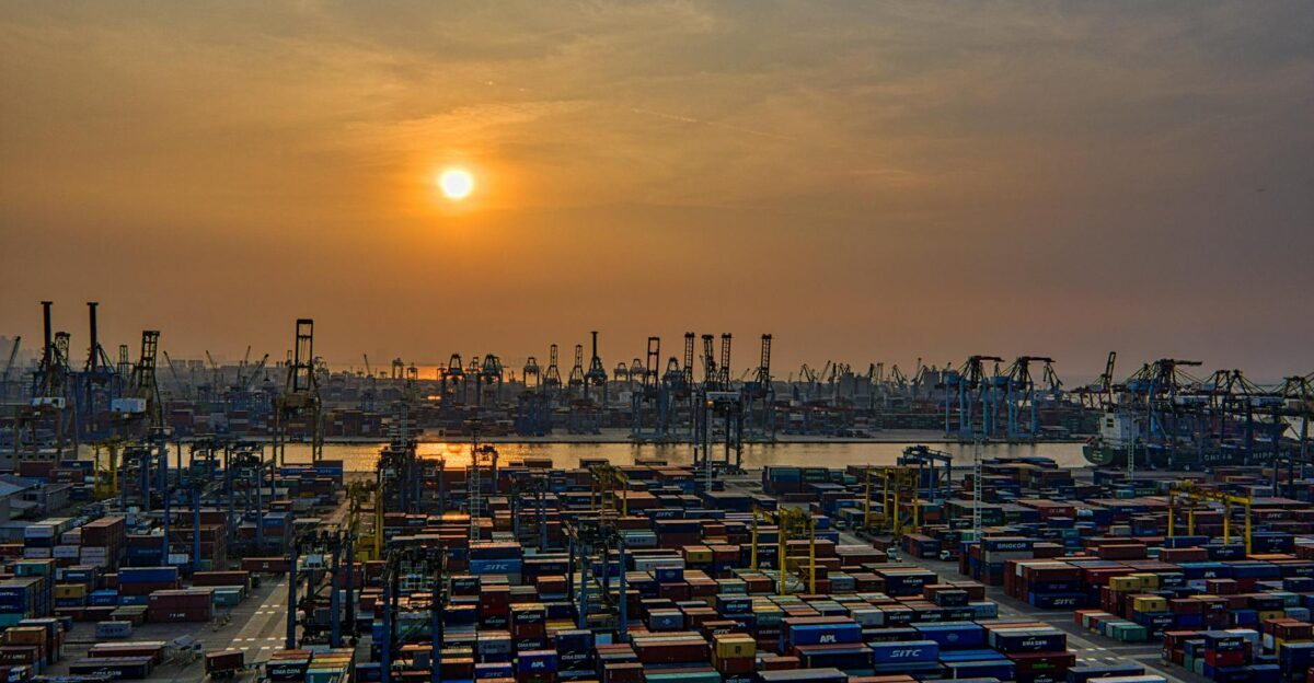 Sunset over a bustling seaport filled with stacked shipping containers and cranes