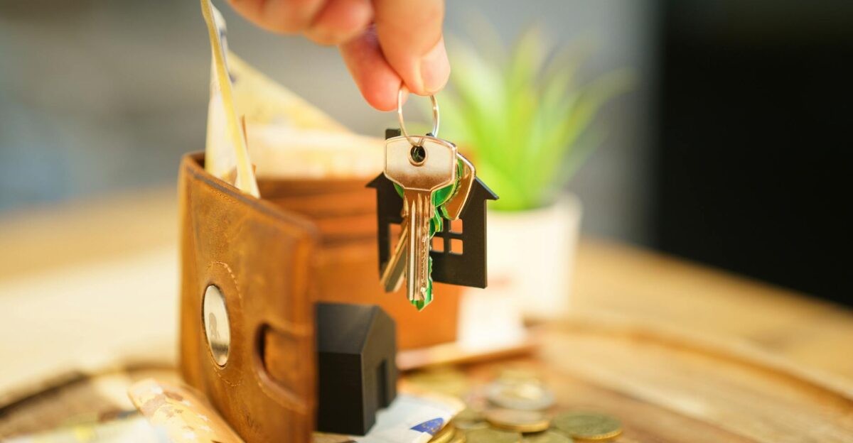 Close-up of hand holding a house key with a wallet and coins symbolizing real estate investment