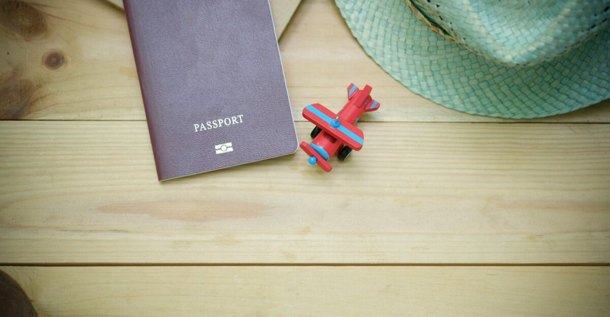 Flat lay of a passport straw hat and toy airplane on a wooden surface