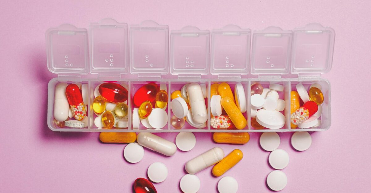 A variety of pills in a weekly pill organizer on a pink background