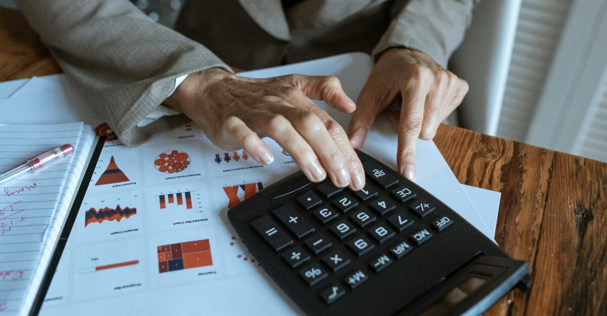 A businessman using a calculator to analyze financial charts and graphs on a desk