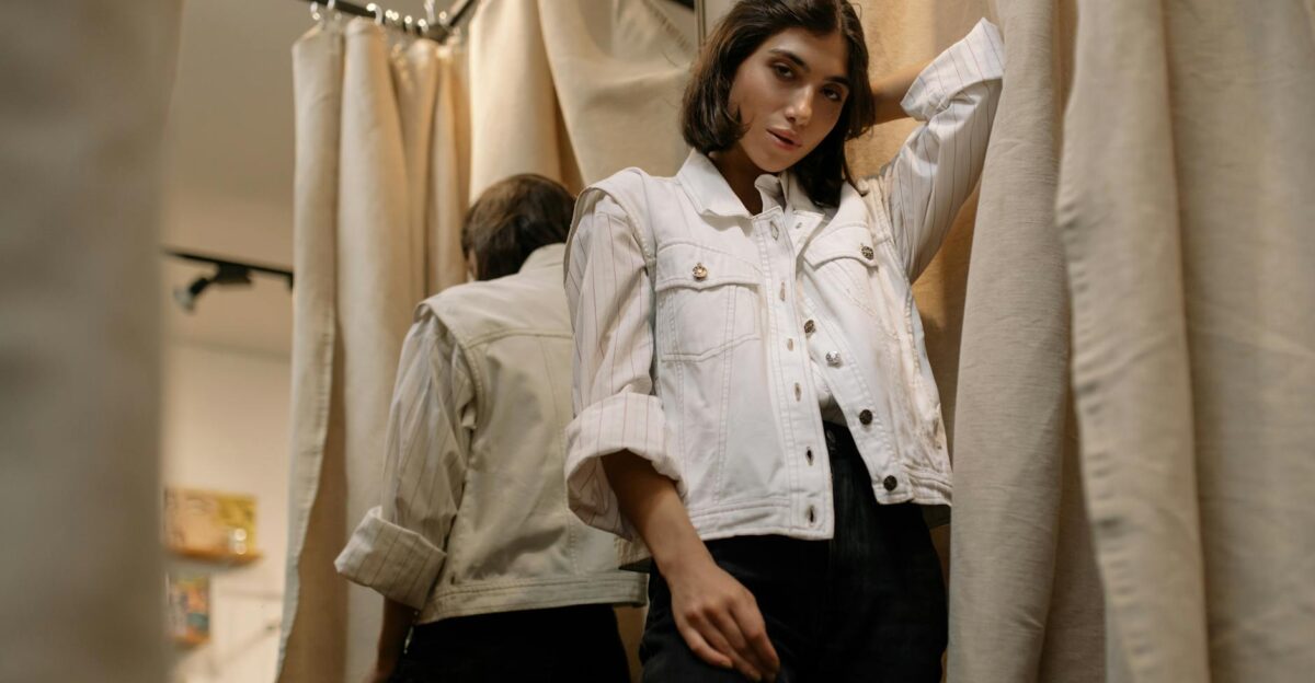 A stylish woman in a casual outfit poses inside a fitting room with curtains in a clothing store