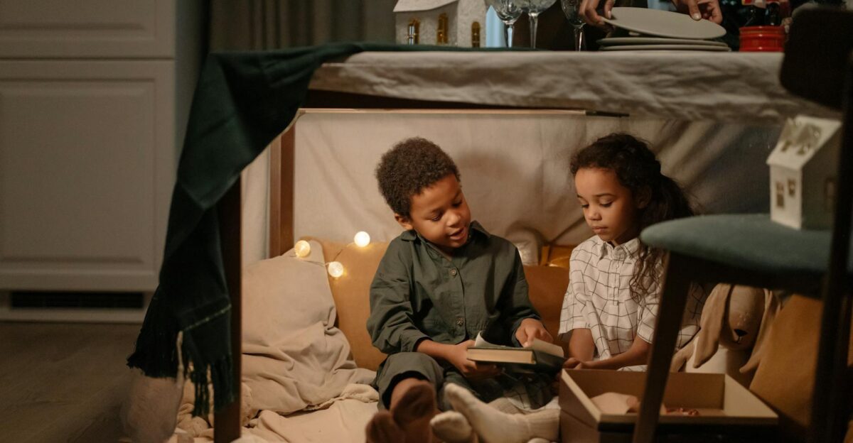 Two children enjoy reading together inside a cozy fort under a table with festive decorations