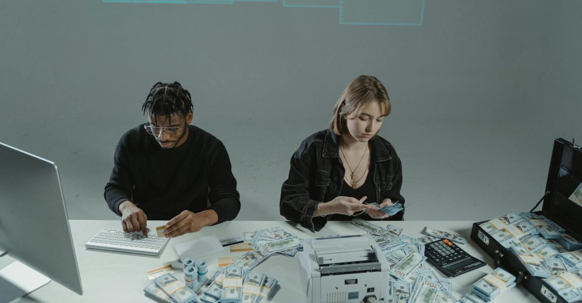 Two people counting money at a desk with computers and cash equipment