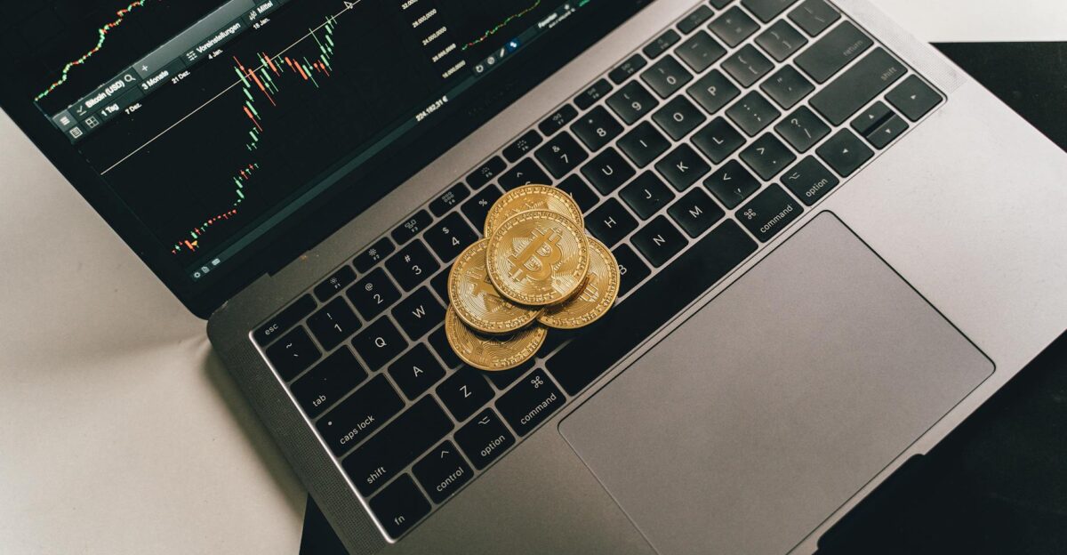 Bitcoin coins placed on a laptop keyboard while a trading chart displays on the screen showcasing digital finance