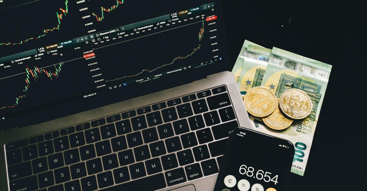 A laptop displaying stock charts with Bitcoin Euros and a cellphone calculator showcasing financial analysis