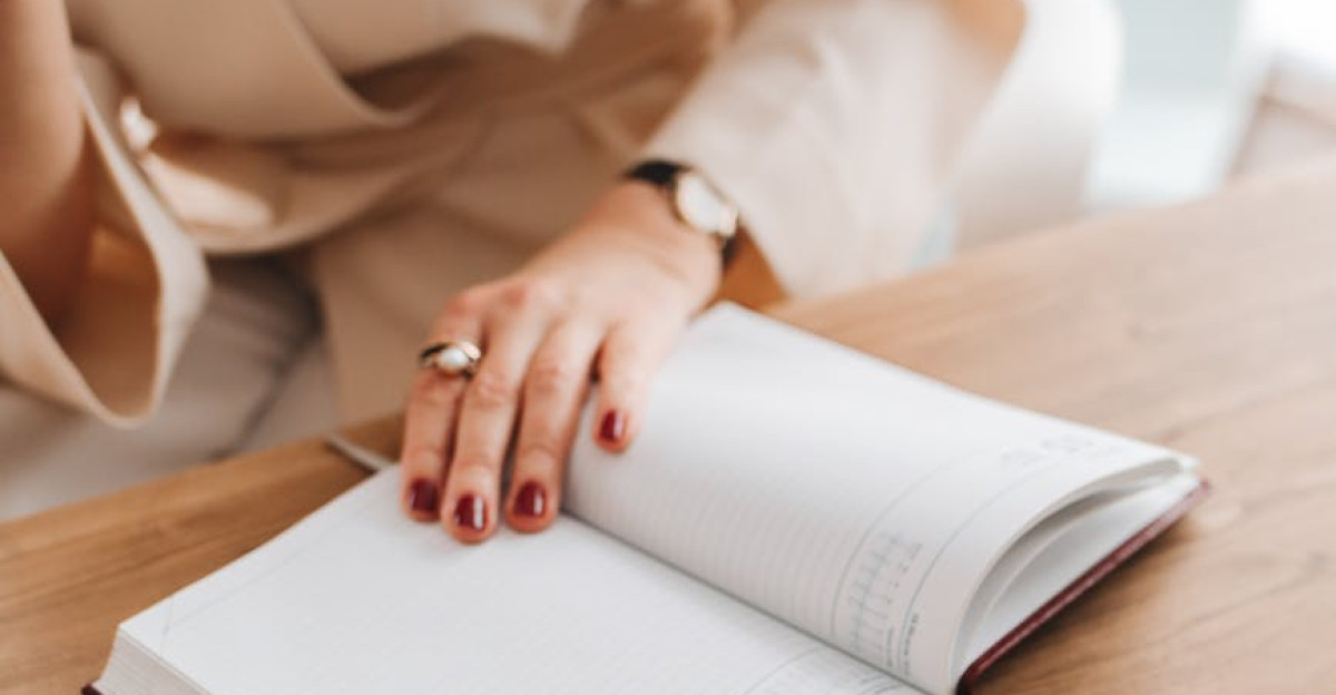Adult woman writing in an open notebook at a wooden desk focusing on reading and note-taking