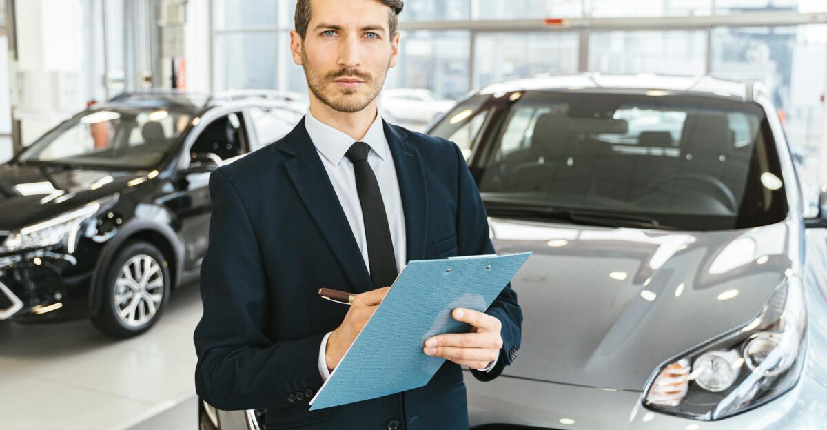 A confident car salesman in a showroom holding a clipboard and pen