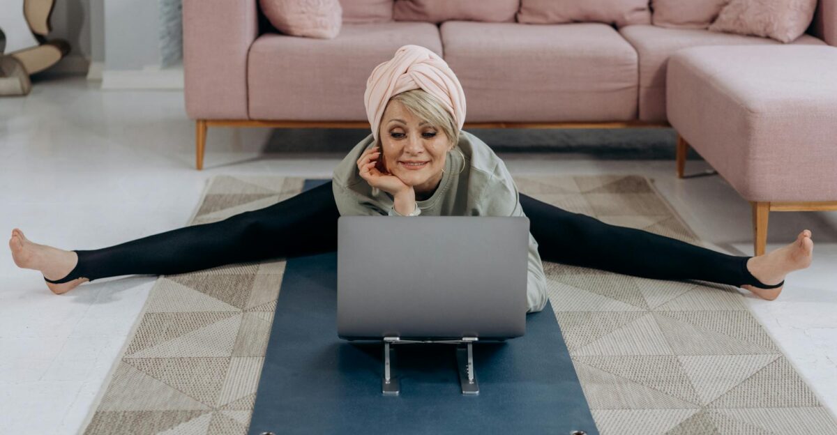 A senior woman enjoys a relaxing yoga session indoors stretching while using her laptop
