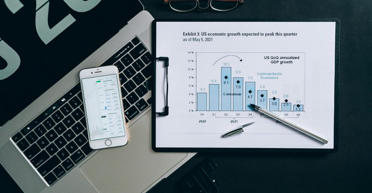 Top view of a financial data analysis setup with laptop smartphone and graph on clipboard