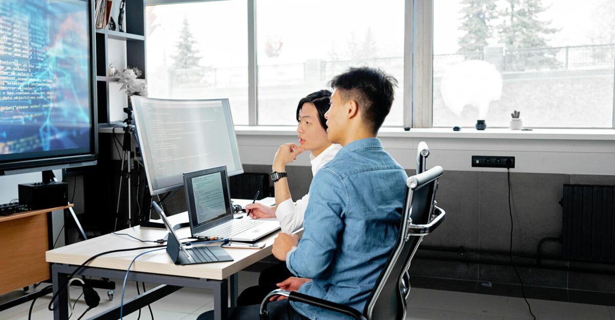 Two men analyzing code on computers in a modern office setting