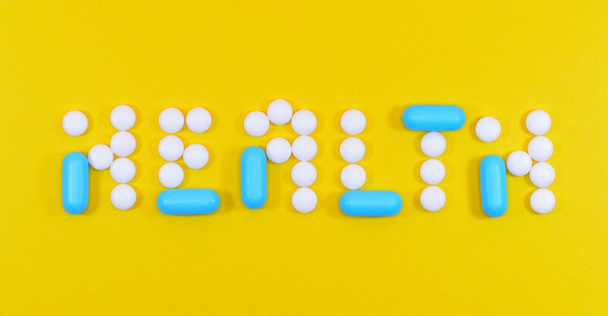 Pills spelling health on a vibrant yellow background symbolizing wellness