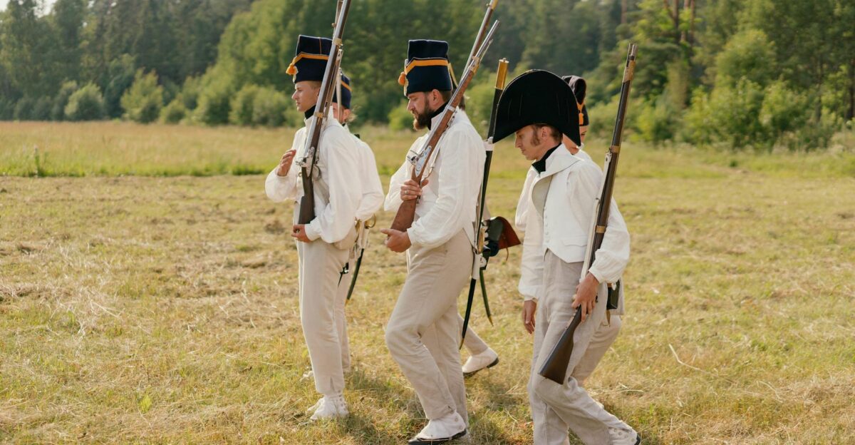 Three soldiers in vintage uniforms reenact a historical march in a grassy field