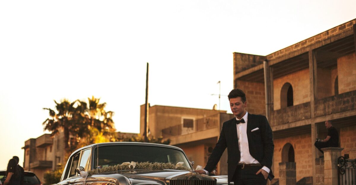 man wearing black suit jacket standing near gray car