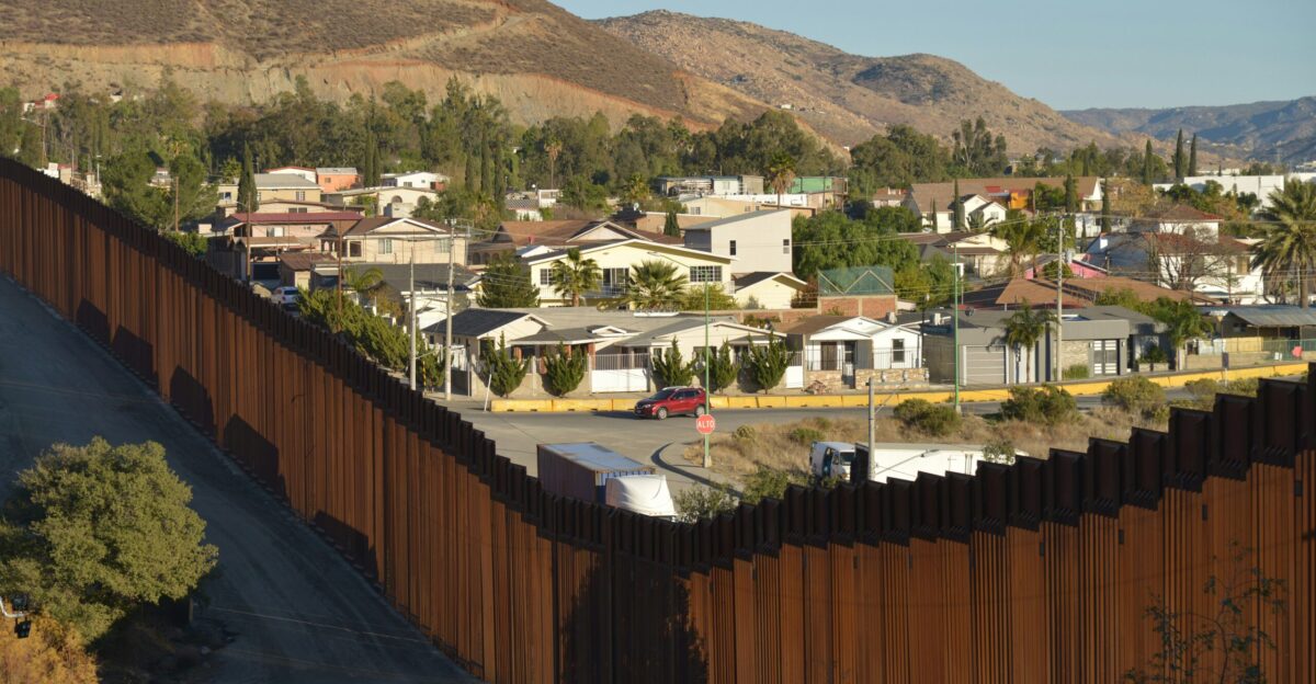 a section of the border fence with houses in the background