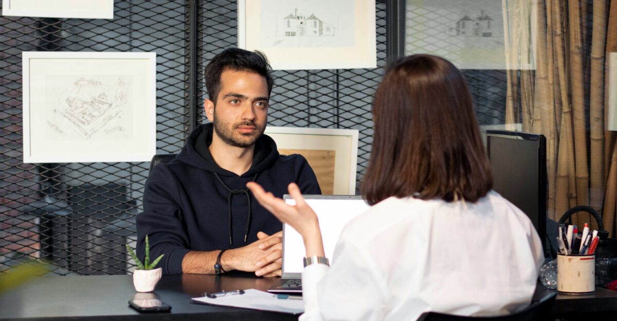 a man sitting at a desk talking to a woman