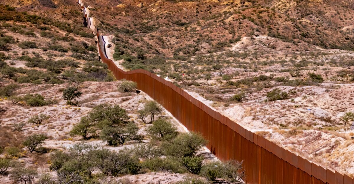 A long metal fence in the middle of a desert