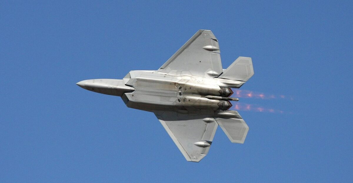 F-22 Raptor fighter jet soaring at high speed with afterburners on a clear blue sky
