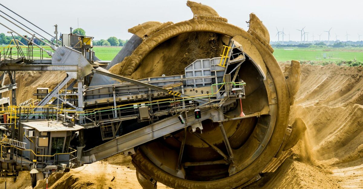 A large bucket wheel excavator working in an open pit mine against a green landscape