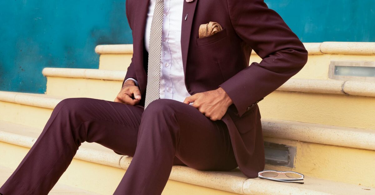 Elegant man in a burgundy suit sitting on steps exuding sophistication and style