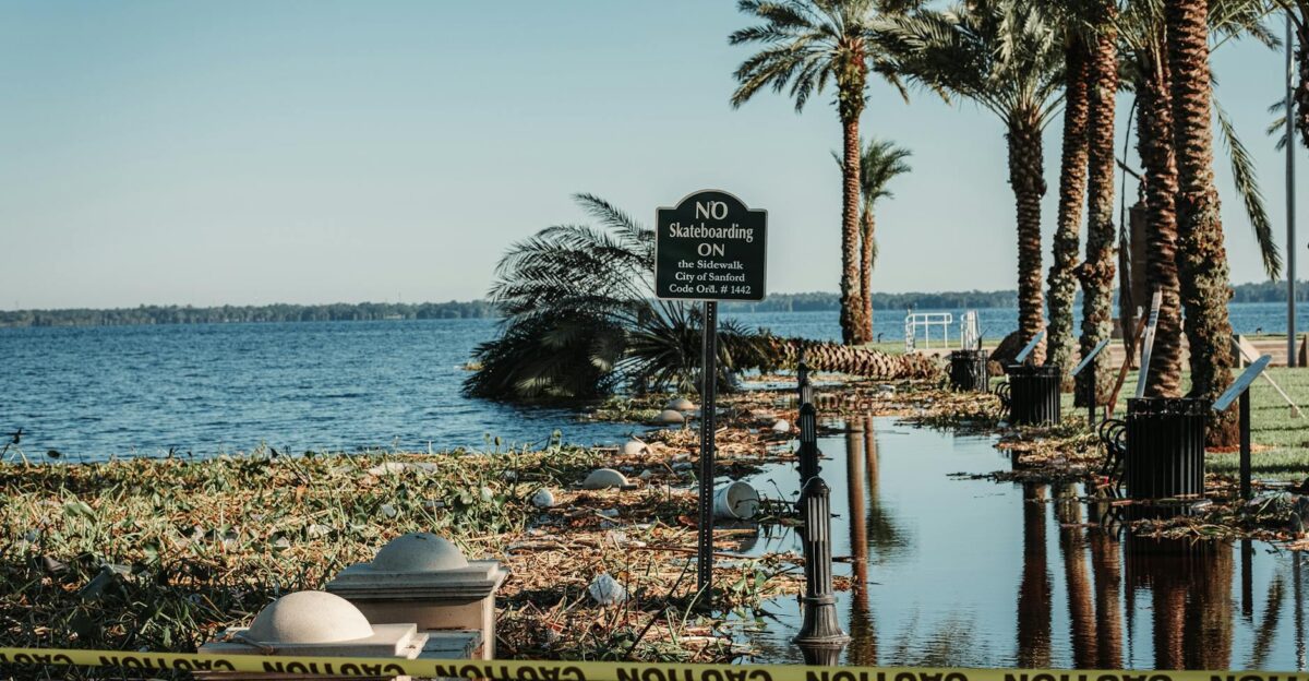 A flooded pathway with caution tape and palm trees by a lake in Sanford Florida
