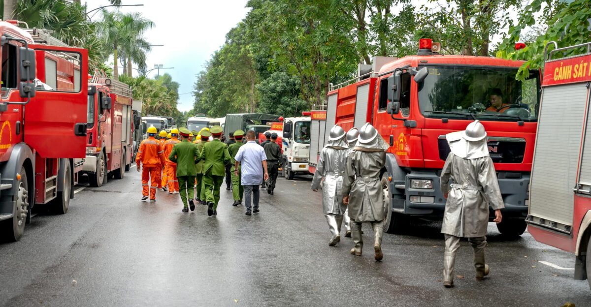 Firefighters in uniforms and fire trucks responding to an emergency on a city street with lush greenery