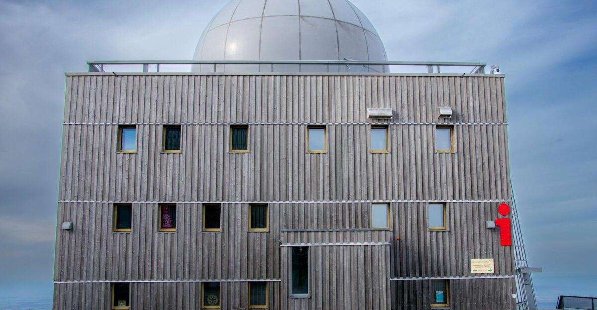 A wooden observatory building with a dome roof against a cloudy sky