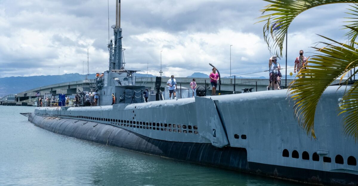 Tourists explore a historic submarine docked at Pearl Harbor Hawaii under a cloudy sky
