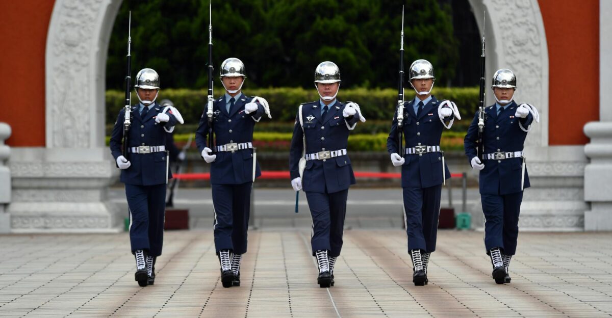 Five uniformed military personnel marching in formation during a ceremonial parade outdoors