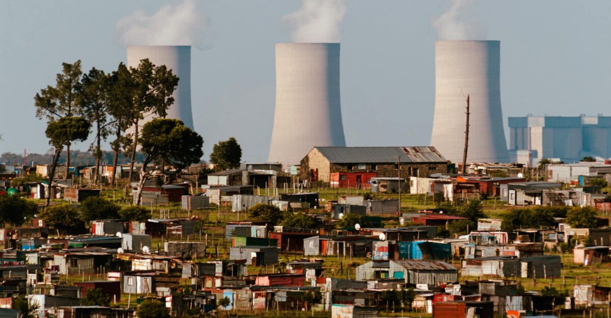 Cooling towers emit smoke over a vibrant South African settlement highlighting industrial impact