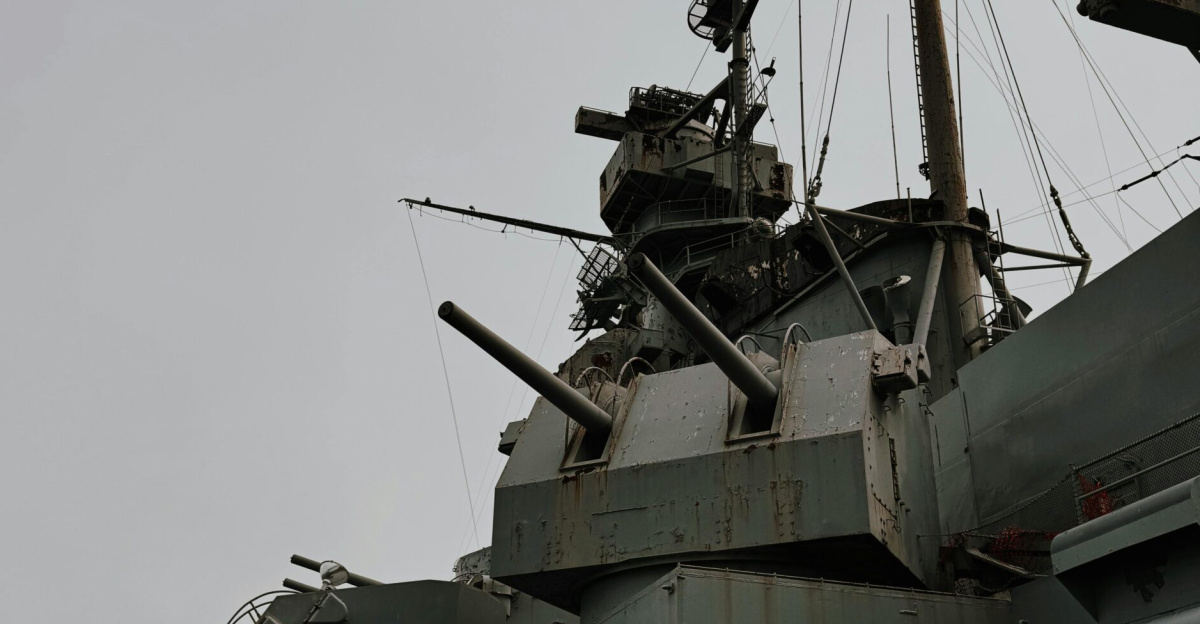Close-up of a battleship's gun turrets and radar systems on a cloudy day.