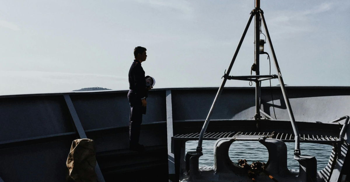 Dramatic silhouette of a sailor standing on a military ship deck against the sky.