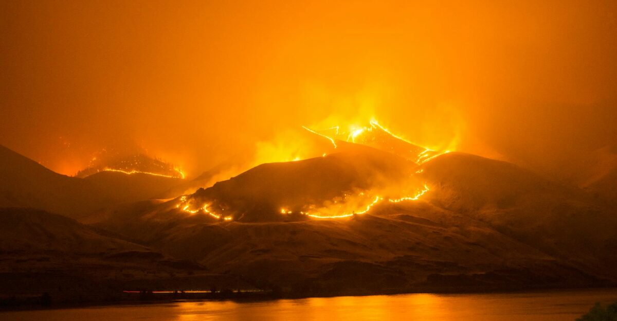 Intense wildfire blazing on hills reflecting over a calm river in Orondo Washington