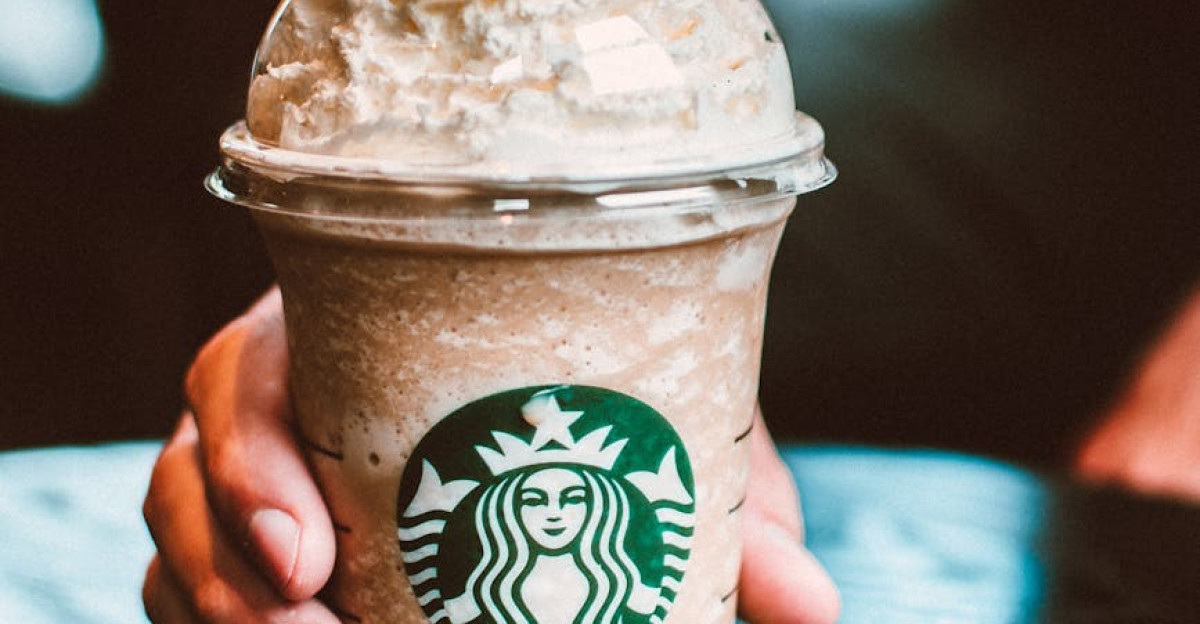 Close-up of a hand holding a Starbucks frappe on a dark wooden table indoors