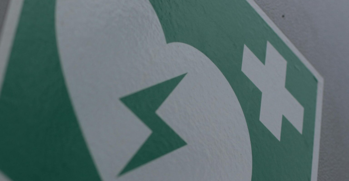 Green first aid sign featuring a broken heart and cross symbol for medical emergency awareness.