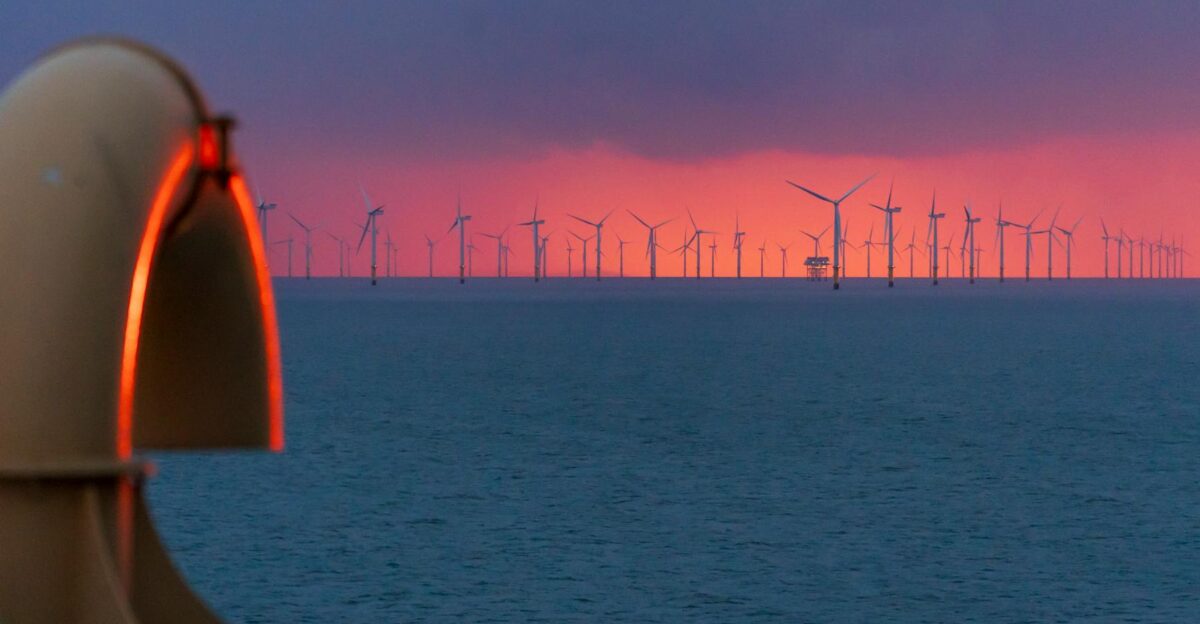 A vibrant sunset over an offshore wind farm captured from the coastline highlighting renewable energy