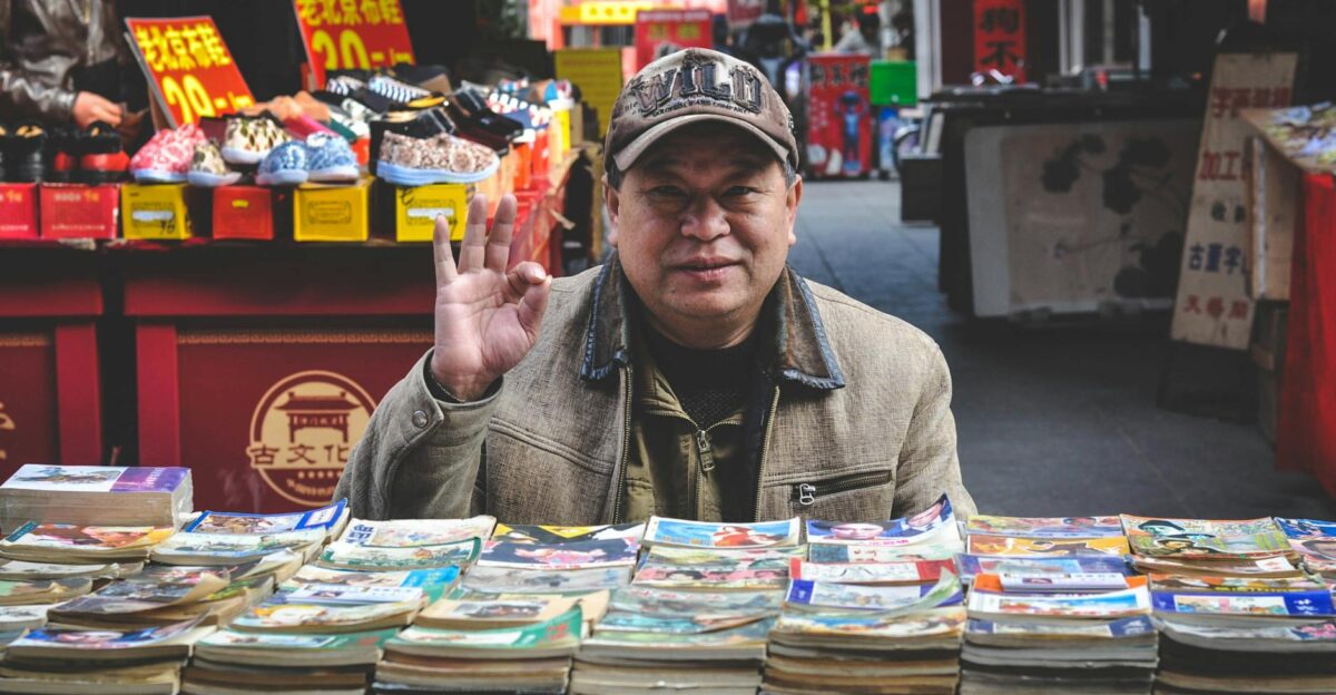 An elderly vendor selling books at a vibrant Tianjin street market