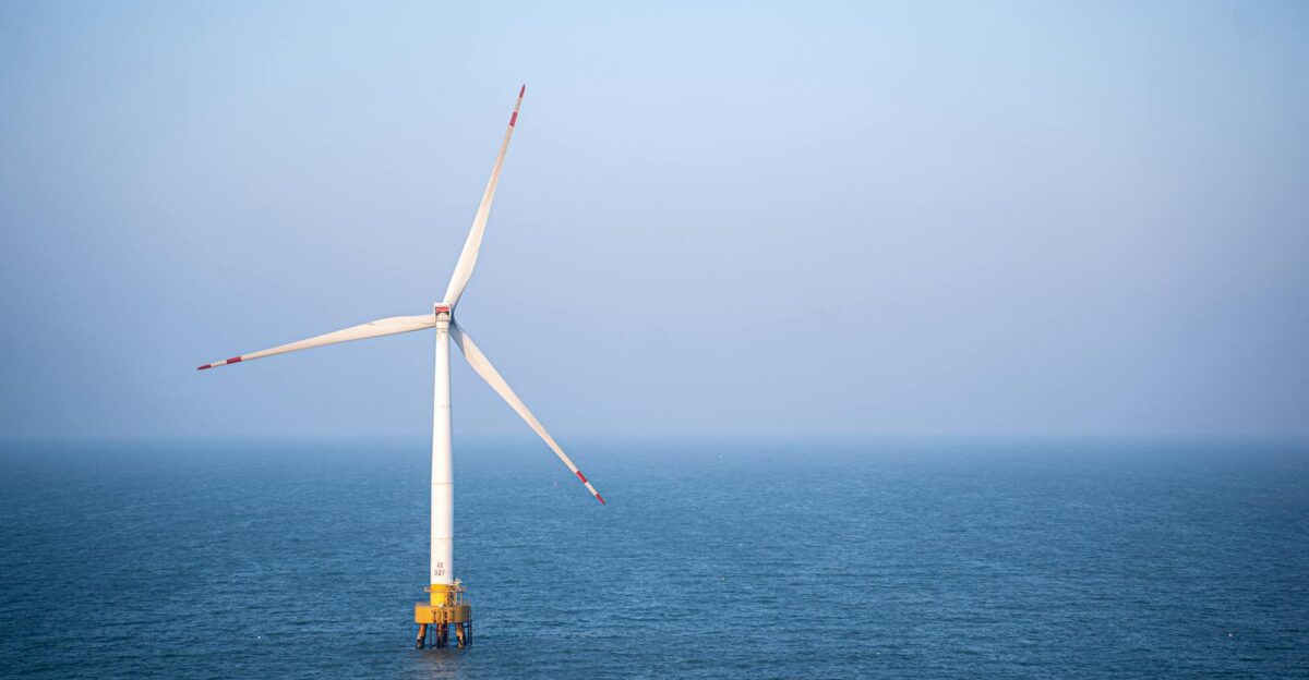 A single wind turbine standing tall in the calm open sea under a clear sky generating renewable energy