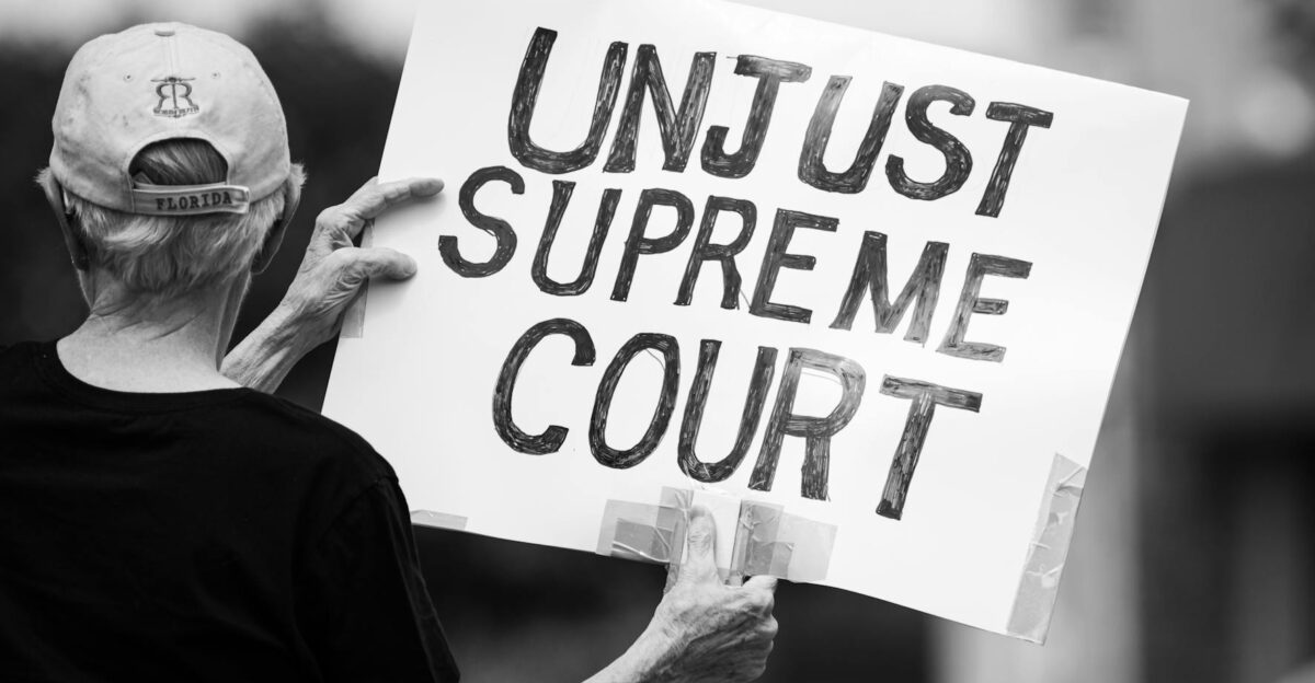 Black and white photo of a protester holding a sign saying Unjust Supreme Court during a demonstration