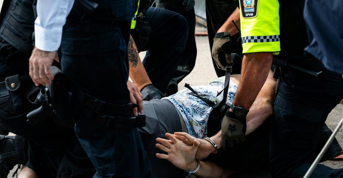 Multiple police officers detain a person on a city street using handcuffs to restrain them