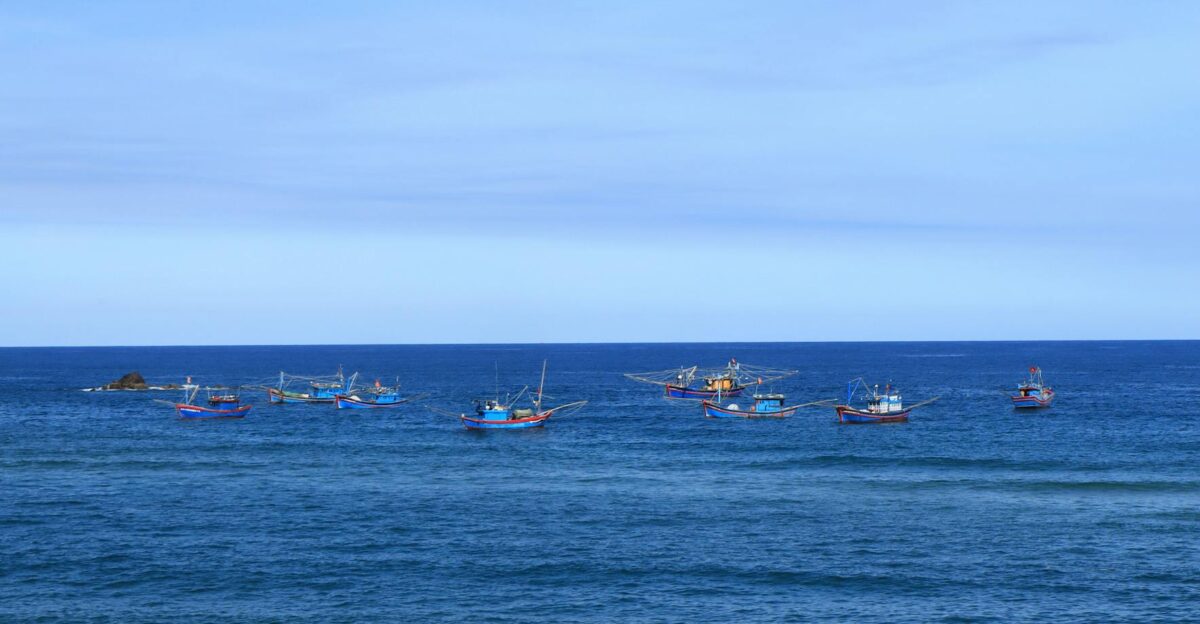 A serene scene of colorful fishing boats floating on the calm blue ocean under a clear sky