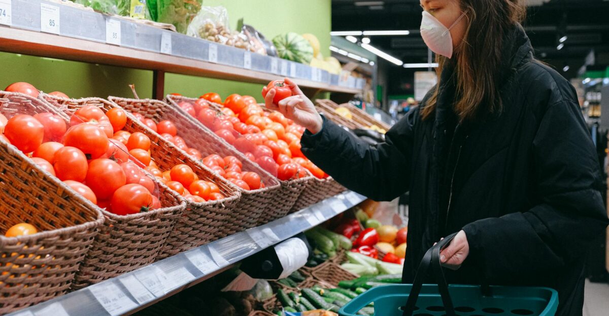 Woman in face mask selecting tomatoes at a grocery store during pandemic